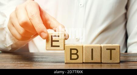 Businessman puts wooden blocks with word Ebit - earnings before interest and taxes. Measure of a firm's profit that includes all incomes and expenses. Stock Photo