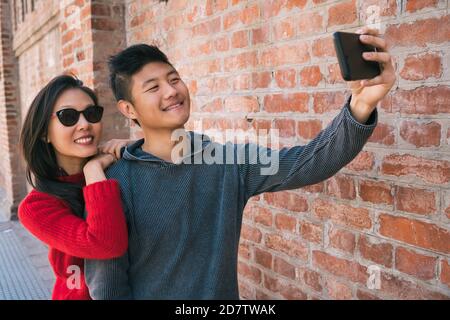 Portrait of a lovely asian couple taking a selfie with mobile phone outdoors in the street. Stock Photo