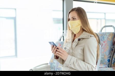 Woman using phone in the bus wearing a face mask Stock Photo