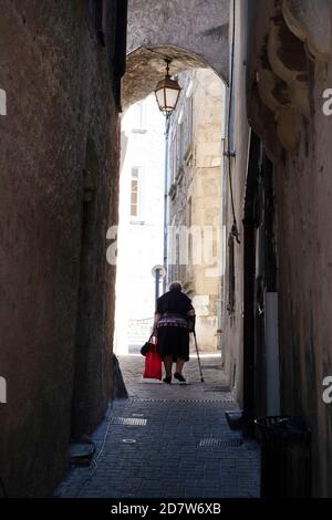 An elderly woman walks down a narrow alley with a shopping cart Stock Photo