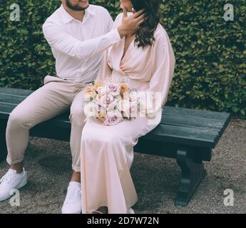 Bridal couple kissing on a bench. Beautiful bride with a bouqet. Wedding photography concept. Stock Photo