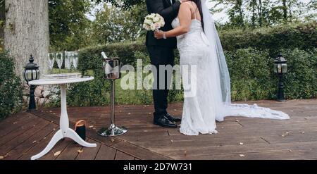 Bridal couple kissing during their official wedding ceremony next to small table with cold champagne and glasses. Stock Photo