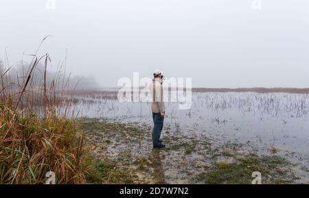 Young caucasian man standing and drinking coffee on fog autumn weather on czech pond landscape Stock Photo