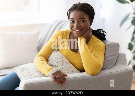 Cheerful African Lady Relaxing On Couch, Holding Pillow And Smiling At Camera Stock Photo