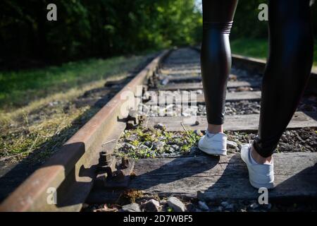 Railway tracks and rusty rails. Shapely slim legs of a young girl. Train tracks underlay. Stock Photo