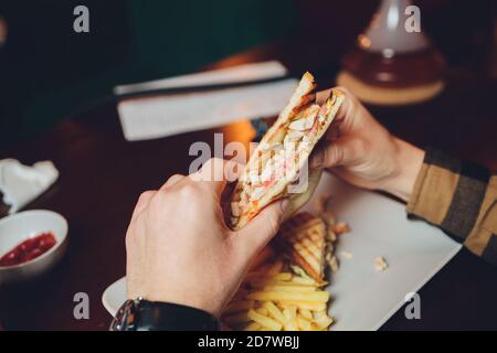 the young man happily prepares to eat a juicy veggie sandwich. sandwich close up, visible chickpea cutlets, tomatoes and salad. Stock Photo