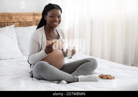 Snack Time. Black Pregnant Woman Eating Cookies And Drinking Milk At Home Stock Photo