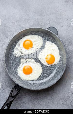 Three sunny side up eggs in skillet isolated on grey concrete background, top view with copy space for design or text Stock Photo