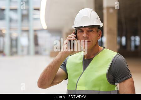 Portrait of professional construction worker speaking by phone and looking at camera while standing on construction site, copy space Stock Photo