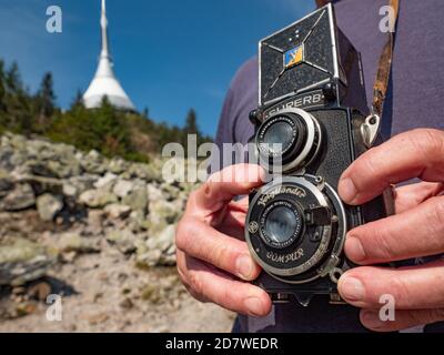 Older photographer man using vintage film camera during trip to Jested mountain.  Wrinkled hands grip the camera body. Stock Photo