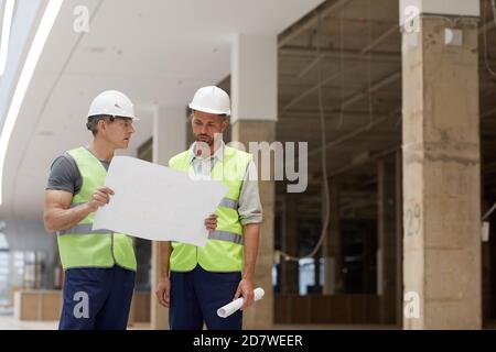 Portrait of two building contractors discussing plans while standing on construction site, copy space Stock Photo