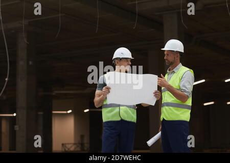 Portrait of two building contractors discussing plans while standing on industrial construction site, copy space Stock Photo