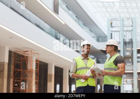 Portrait of two mature building contractors discussing work while standing on construction site, copy space Stock Photo