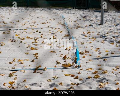 Closed beach volleyball court in fall season. Autumn weather and fallen leaves on white playground sand. Stock Photo