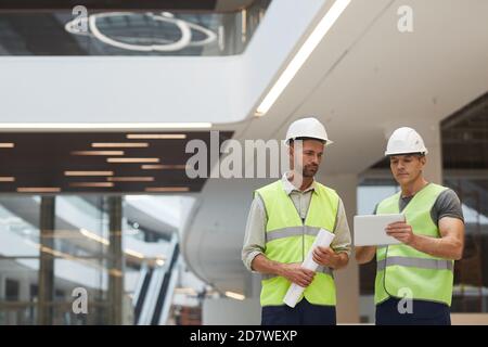 Waist up portrait of two mature building contractors using digital tablet while standing in office building at construction site, copy space Stock Photo