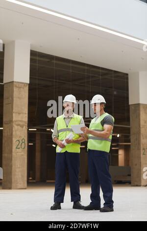 Vertical full length portrait of two building contractors using digital tablet while standing at construction site, copy space above Stock Photo