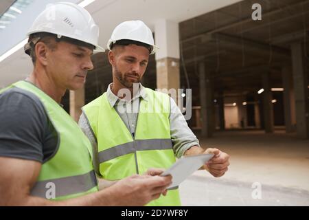 Waist up portrait of two professional building contractors using digital tablet while standing at construction site, copy space Stock Photo