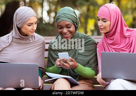 Muslim Lady Using Smartphone Learning Online With Friends Sitting Outdoor Stock Photo