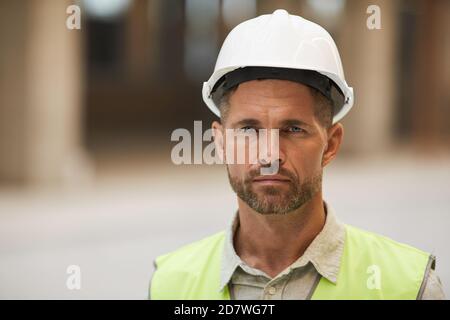 Close up portrait of mature construction worker wearing hardhat and looking at camera while standing at construction site, copy space Stock Photo