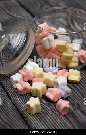 Marshmallows of different colors. They lie in a glass jar. Against the background of black pine boards. Stock Photo