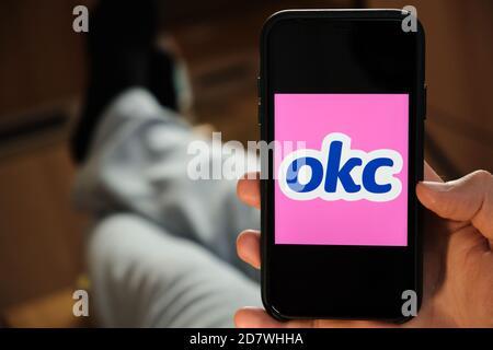 OKS logo on the screen of mobile phone in mans hand. Application for dating and acquaintance. Man is laying on the sofa and looking for partner in the Stock Photo