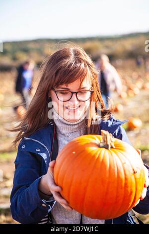 A young woman holding and looking at a pumpkin she's just picked, looking happy with her choice, ready for Halloween. Stock Photo