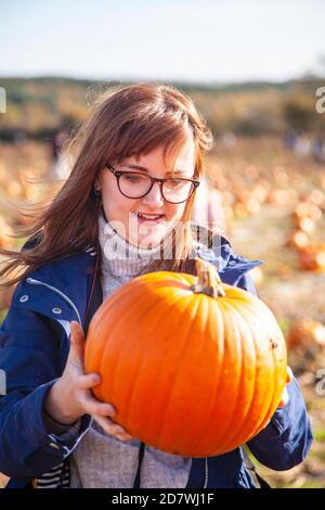 A young woman holding and looking at a pumpkin she's just picked, ready for Halloween. Stock Photo