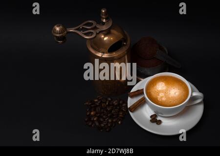 Cup of aroma coffee, coffee beans, aged manual coffee grinder, ground coffee, cinnamon sticks on black background Stock Photo