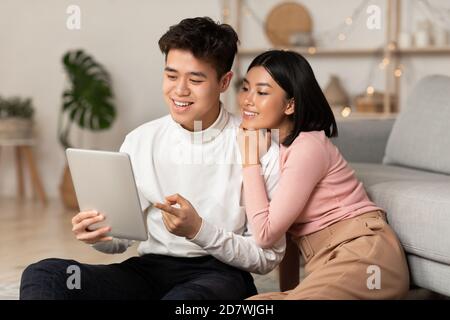 Young Asian Spouses Relaxing Using Digital Tablet Browsing Internet Indoors Stock Photo