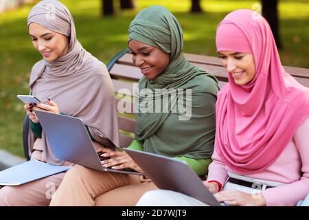 Muslim Students Women Using Gadgets Learning Online Sitting In Park Stock Photo