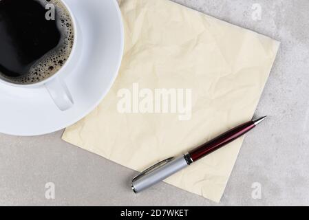 A cup of coffee with a wrinkled napkin and pen on a light gray table. Stock Photo