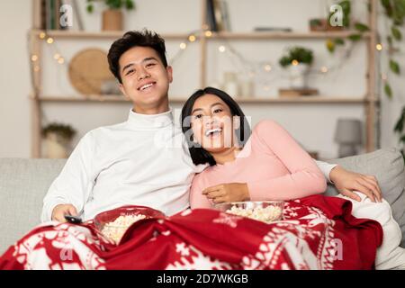 Happy Chinese Couple Watching TV Sitting On Couch At Home Stock Photo