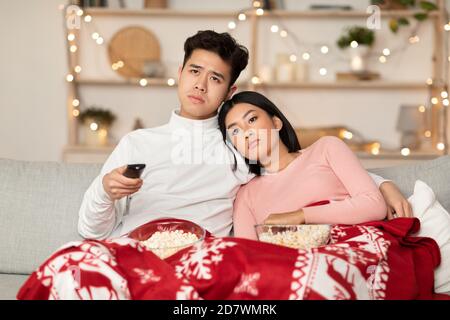 Bored Asian Couple Watching TV Celebrating Christmas At Home Stock Photo