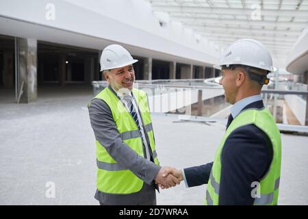 Waist up portrait of smiling mature businessman shaking hands with partner after investment deal at construction site, copy space Stock Photo