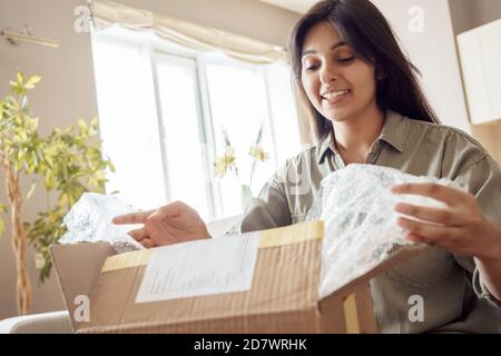 Smiling indian woman shopper customer opening post parcel box at home. Stock Photo