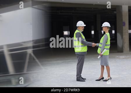 Side view portrait of smiling businessman shaking hands with female partner after investment deal at construction site, copy space Stock Photo
