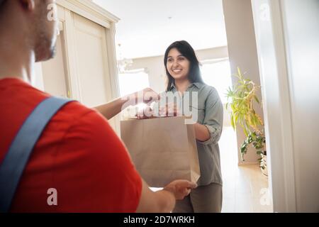 Indian woman customer takes delivery bag from courier at home. Stock Photo