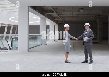 Full length side view portrait of smiling businesswoman shaking hands with partner after investment deal at construction site, copy space Stock Photo