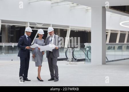 Full length portrait of successful business people looking at plans while standing at construction site indoors, copy space Stock Photo