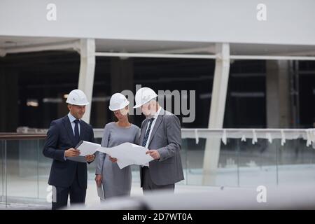 Portrait of three successful business people wearing hardhats and holding plans while inspecting construction site, copy space Stock Photo