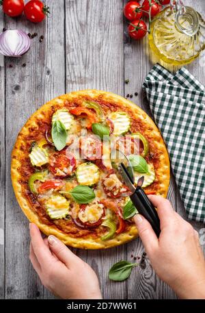 Freshly backed vegetarian pizza being cutting by womans hands Stock Photo