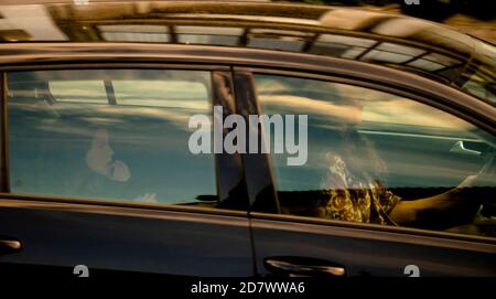 Belgrade, Serbia - October 02, 2020: Woman driving a car and a little girl riding on a back seat of it, through window with reflections and blurs Stock Photo