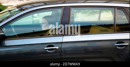 Belgrade, Serbia - October 02, 2020: Young woman driving a car, alone, through window with reflections and blurs Stock Photo