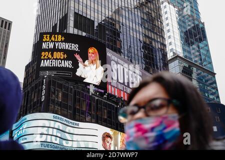 A woman wearing a face mask walks past a Lincoln Project Billboard that depicts Ivanka trump presenting the number of New Yorkers and americans who have died of Covid-19 and Jared Kushner next to a Vanity Fair quote. Stock Photo