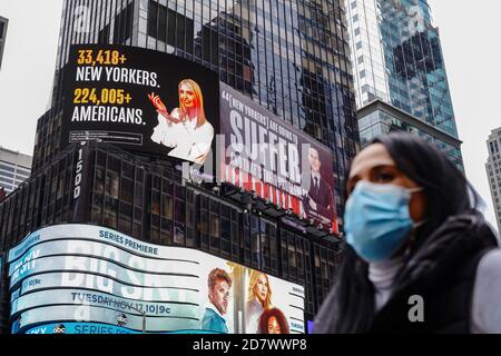 A woman wearing a face mask walks past a Lincoln Project Billboard that depicts Ivanka trump presenting the number of New Yorkers and americans who have died of Covid-19 and Jared Kushner next to a Vanity Fair quote. Stock Photo