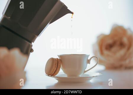 Coffee pouring to a white porcelain cup with a macaron from a black coffeemaker Stock Photo