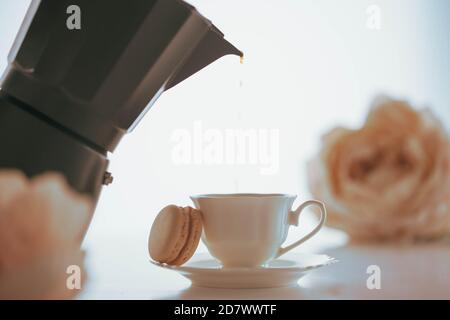 Coffee pouring to a white porcelain cup with a macaron from a black coffeemaker Stock Photo