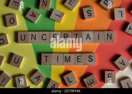 Uncertain Times, words in wooden letters surrounded by random alphabet blocks on a colorful background Stock Photo