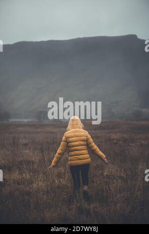 Woman walking wearing yellow down jacket, enjoying landscape travel lifestyle Stock Photo