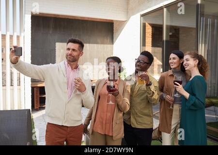 Waist up portrait of multi-ethnic group of friends taking selfie photo while enjoying party standing at outdoor terrace Stock Photo
